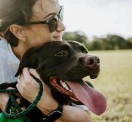 A woman in sunglasses hugging a brown dog