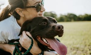 A woman in sunglasses hugging a brown dog
