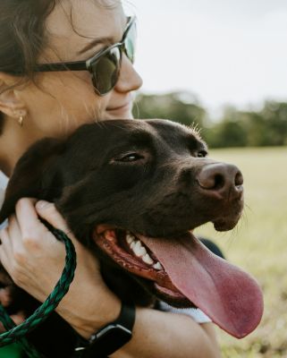 A woman in sunglasses hugging a brown dog