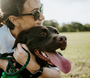 A woman in sunglasses hugging a brown dog