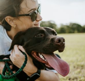 A woman in sunglasses hugging a brown dog
